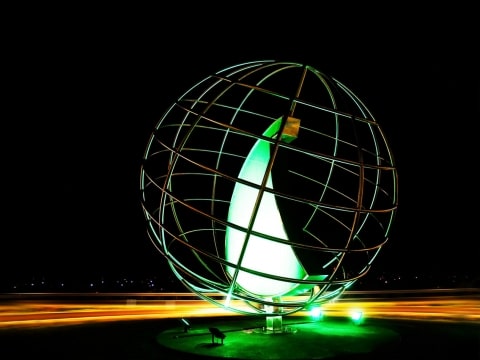 Kreisverkehrskulptur Hammerer Aluminium Ranshofen bei Nacht | Kugelform aus Alu-Stangen-Gitter mit grün beleuchteter Haiflosse | Svoboda