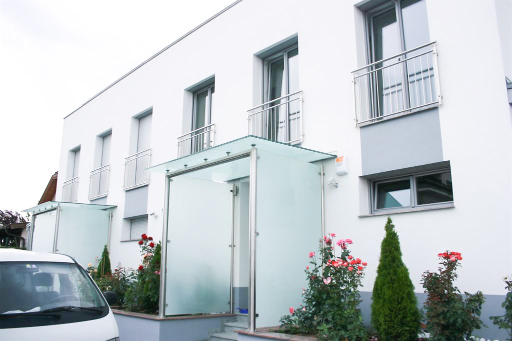 Vordach Niro 10 a | Edelstahl-Mattglas-Vordach mit Windfang seitlich bei Wohnungsanlage | Svoboda