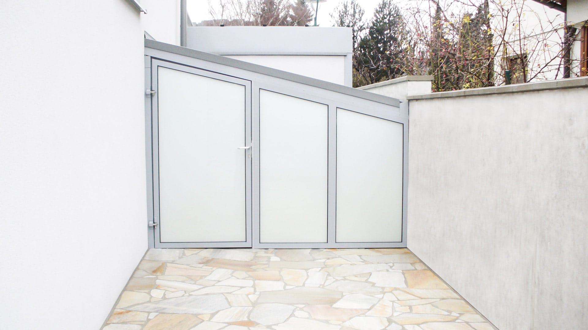 S 01 b | Geräteeinhausung aus grauem Alu und Fixglas mit Tür zwischen Haus und Gartenmauer | Svoboda